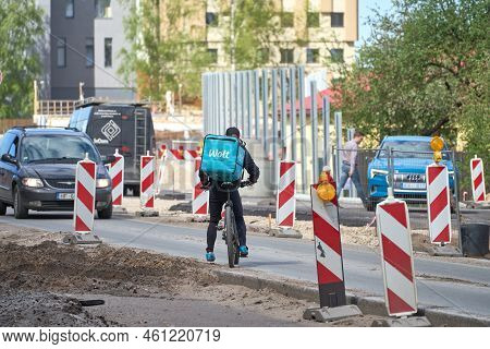 Riga, Latvia - May 13, 2022. A Cyclist From Wolt Food Delivery Company Trying To Cross Road Under Re