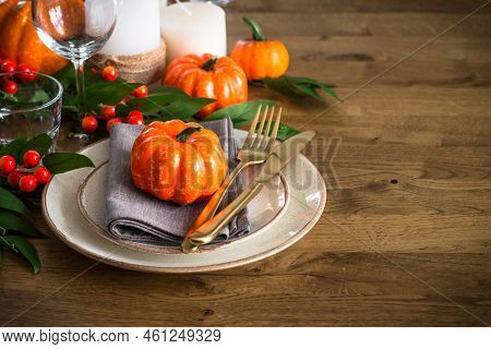 Autumn Table Setting With Plate, Pumpkin And Candles At Wooden Table. Thanksgiving Food Festive Dinn