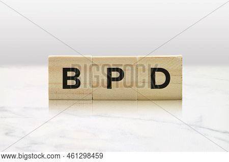 Closeup Of Wood Tiles Spelling Out Bpd Against A Modern White Marble Background.