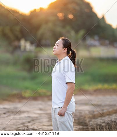 Asian Man Long Hair Stands And Relax On The Dry Field In Golden Twilight Time.