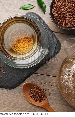 Cup Of Freshly Made Aromatic Buckwheat Tea And Granules On Wooden Table, Flat Lay