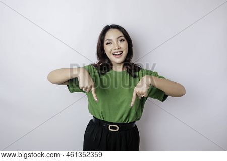 Excited Asian Woman Wearing Green T-shirt Pointing At The Copy Space Downside Her, Isolated By White