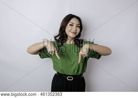Excited Asian Woman Wearing Green T-shirt Pointing At The Copy Space Downside Her, Isolated By White