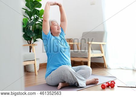 Asian Elderly Woman Sitting At Home Exercising, Doing Exercises According To Online Fitness Trainers