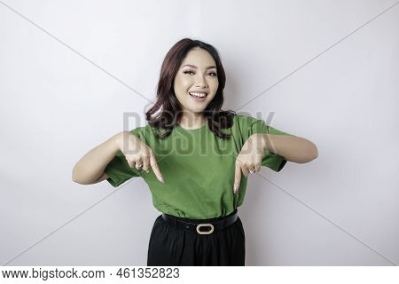 Excited Asian Woman Wearing Green T-shirt Pointing At The Copy Space Downside Her, Isolated By White