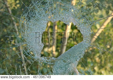 A Hole In The Glass Or Window. Broken And Pierced Window Overlooking The Green Background. A Hole Fr