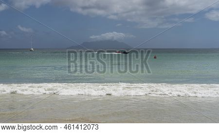 Tropical Seascape. Surf Waves Are Foaming On The Sandy Beach. The Boat Rushes Across The Turquoise O