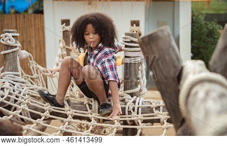 African American Kid Girl Playing On A Rope-ladder Web In A Playground.