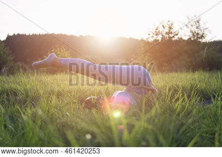 A Girl In Blue Leggings Does A Stretching Throwing Her Legs Over Herself Lying In A Park In The Fres