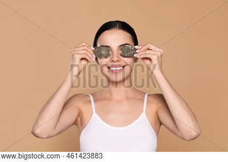 Beautiful Young Woman Putting Green Tea Bags On Skin Around Eyes Against Beige Background