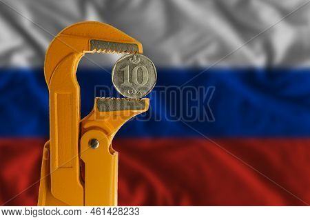 Kyrgyzstani Ten Som Coin Clamped In An Orange Plumber Wrench On The Background Of The Russian Flag. 