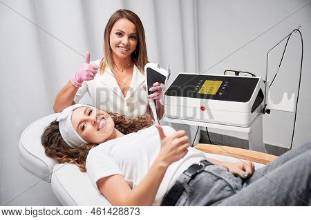 Smiling Cosmetologist And Young Woman Showing Approval Gesture After Laser Skincare Procedure. Beaut