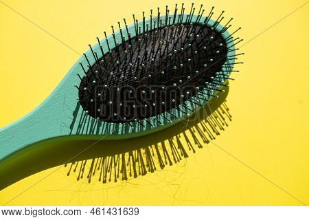 Green Comb With Fallen Hair On The Yellow Background. Baldness And Hair Loss Problem