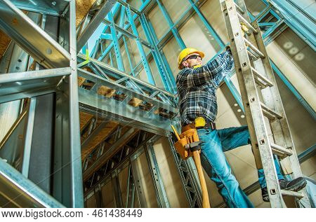 Caucasian Contractor Climbing A Ladder Inside Steel House Frame Construction During Its Development 