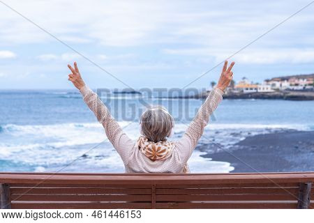 Rear View Of Senior Woman Wearing Headphones Sitting On Outdoors Bench At Sea Looking At Horizon Ges
