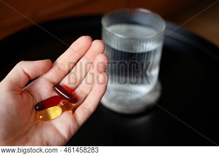 Hand Holding Omega 3 6 9, Vitamine E And D, Evening Primrose Supplement Capsules Above Table With Gl