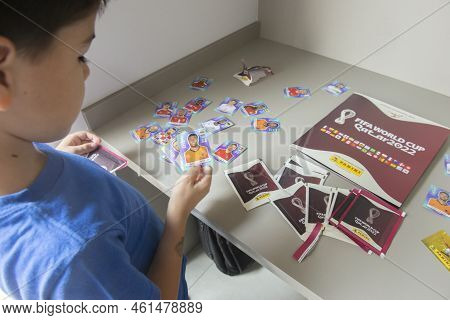 Bauru, Brazil - 12.09.22: Back View Of Boy Opening Sticker Packs To Paste In Panini Fifa World Cup 2