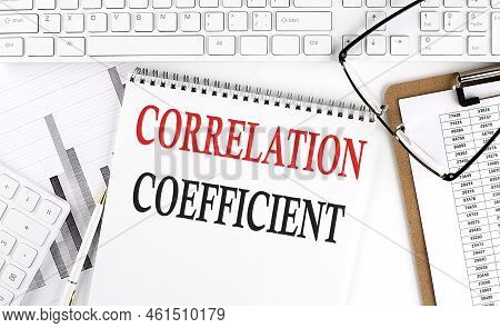 Text Correlation Coefficient On Office Desk Table With Keyboard, Notepad And Analysis Chart On A Whi