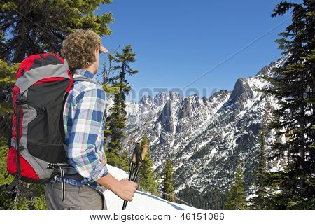 Hiker admiring the view on the snowy mountains of the Kangaroo ridge from the Washington Pass overlook in the North Cascades Range, with the melting snow on a warm spring day
