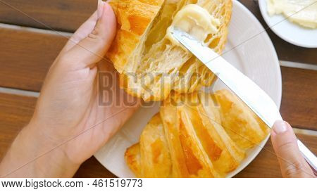 Traditional French Breakfast - Woman Hands Cut A Fresh Croissant And Spreading Butter Inside On Brea
