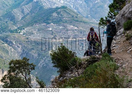 Hikers Going Down A Path In Sierra De Tejeda And Almijara With A Mountain Wall In The Background