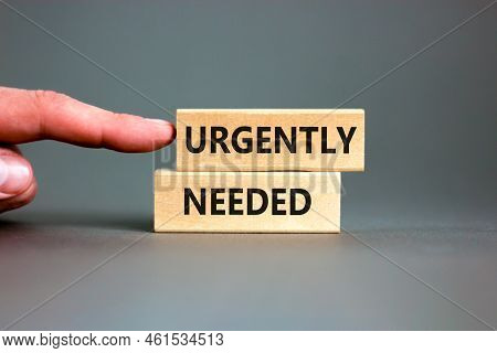 Urgently Needed Symbol. Concept Words Urgently Needed On Wooden Blocks On A Beautiful Grey Table Gre