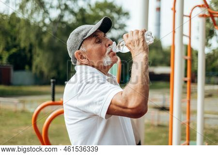 Healthy Mature Man In His 60th In Sports T-shirt Drinking Bottled Water To Restore Water Balance Aft