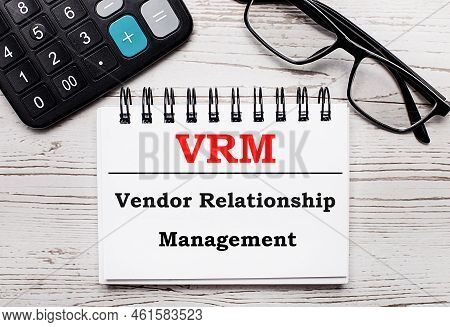 On A Light Wooden Table Calculator, Glasses And A Blank Notepad With The Text Vrm Vendor Relationshi