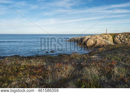 View Of The Sea And Cliffs With The Red And White Lighthouse At Praia Pequena Beach At Wild Vicentin