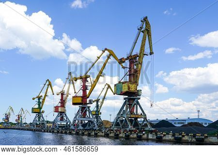 Bulk Cargo Terminal In Port With Many Shore Cranes And Piles Of Coal And Wood Chips