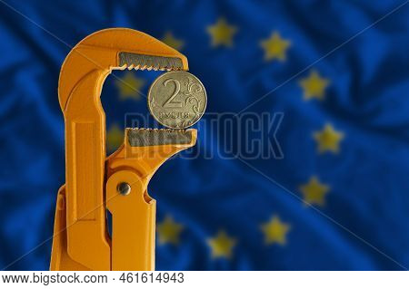 Russian Two Rubles Coin Clamped In An Orange Plumber Wrench On The Background Of The European Flag. 