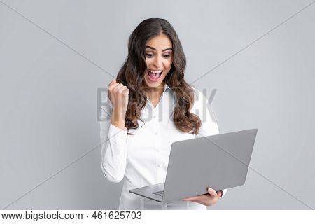 Portrait Of A Cheerful Young Casual Girl Standing Isolated Over Gray Background, Using Laptop Comput