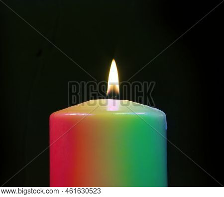 Rainbow Candle Burning On A Black Background With Wax Just Strating To Drip