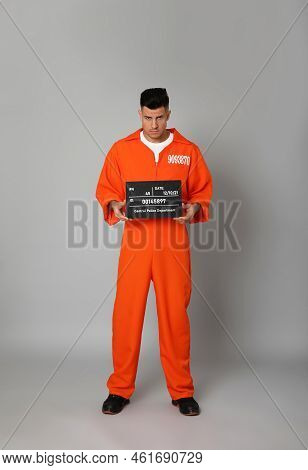 Prisoner In Orange Jumpsuit With Mugshot Letter Board On Grey Background
