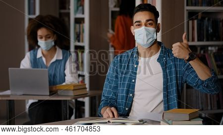 Students In Library Young Indian Guy In Protective Mask Sits At Desk Doing Homework Preparing For Ex