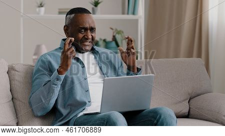 Mature African American Man Sitting At Home Looking At Laptop Screen With Hope Crossed Fingers Prayi