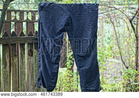 One Blue Crumpled Cloth Pants Hangs On A Wire In The Street Among Green Vegetation