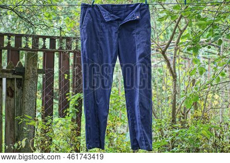 One Blue Crumpled Cloth Pants Hangs On A Wire In The Street Among Green Vegetation