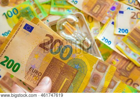 Electricity Cost .electric Light Bulb In Hand On Euro Bills Background. Rising Electricity Prices.pa