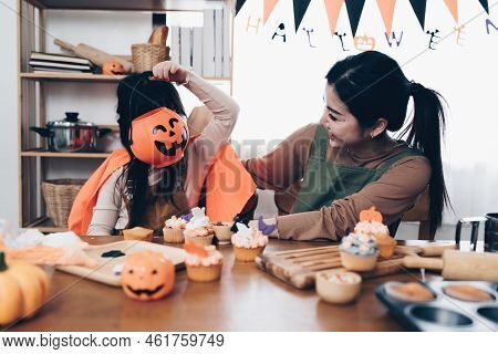 Young Girl And Mother At Halloween Making Treats And Cupcake On Table. Happy Halloween Day