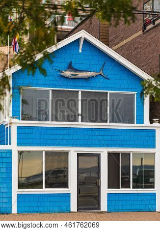 Bright Blue House In Sunlght Decorated With Fish On The Top. Facade Of A Colorful House With Door An