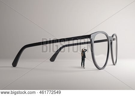 Thoughtful Young Female Looking Through Abstract Huge Glasses On Gray Background. Clear Business Vis