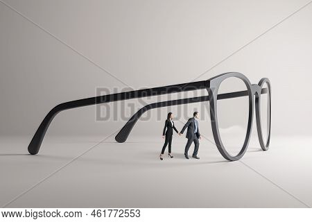 Thoughtful Young Businesspeople Holding Hands And Looking Through Abstract Huge Glasses On Gray Back