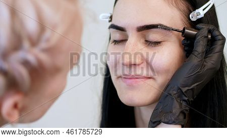 Beauty Saloon. Close-up, A Beautician In Black Rubber Gloves, Gently Combs The Eyebrows Of The Clien