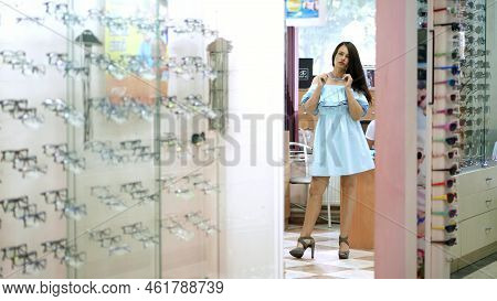 Sexy Young Woman In Dress Choosing New Glasses At Optician Retail Store. Young Woman With Eyeglasses