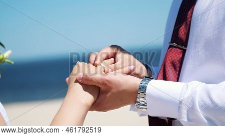 Close-up, The Bride And Groom Wear Rings To Each Other, Against The Background Of The Sea, Sand And 