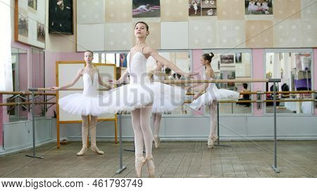 In Ballet Hall, Girls In White Ballet Skirts Are Engaged At Ballet, Rehearse Turning, Young Ballerin