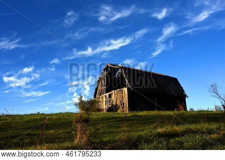 Dusk Settles Over Hillside Barn.  The Last Of The Sunlight Captures The Rustic Wooden Boards And Gap