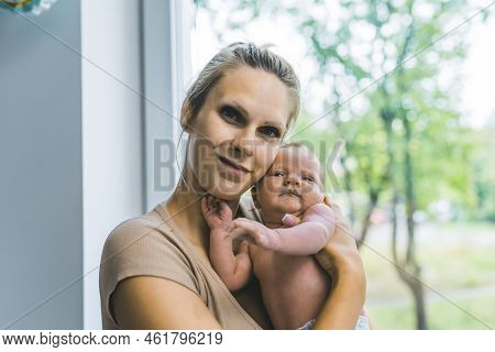 Caucasian Woman With Blond Hair Holding Her Baby Up To Her Face Hugging It Showing It To The Camera 