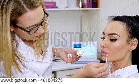 Medical Office, Doctor Puts On Patient Lips A Cosmetic Cream With A Cotton Swab, After Injections Of